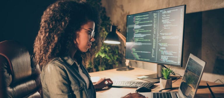 woman working on two computer screens with lines of code visible - External network penetration testing