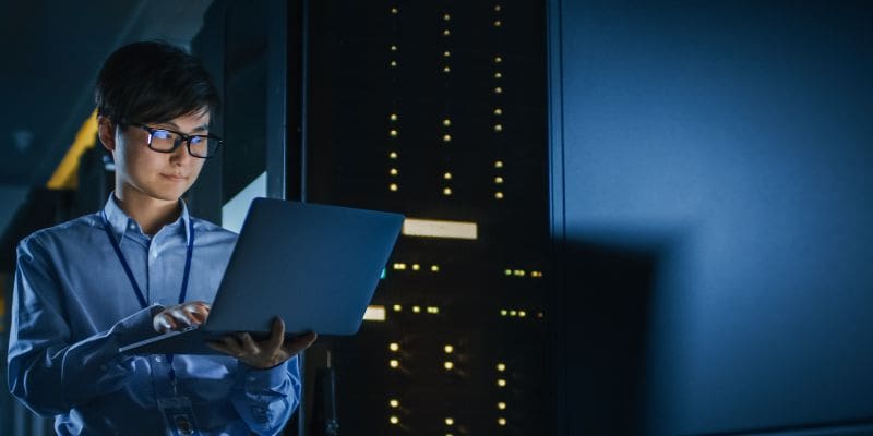 Person holding a laptop in a dark technology room