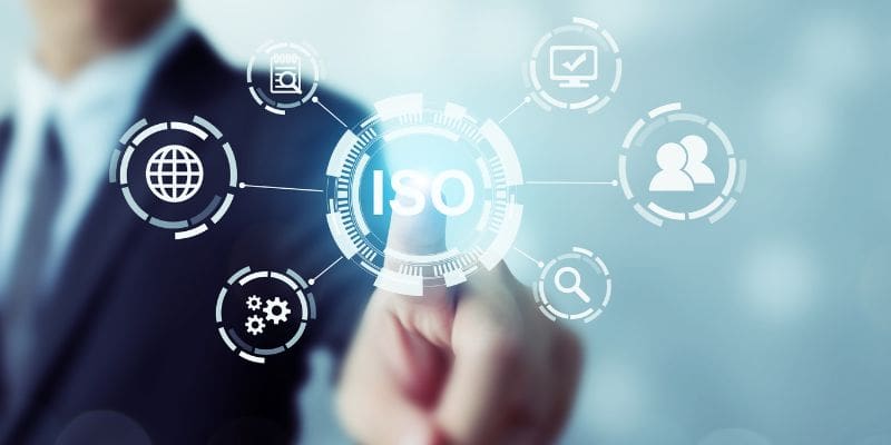 ISO 27001 Compliance: Complete Guide 1 man out of focus touching ISO on screen overlay - ISO 27701 Compliance