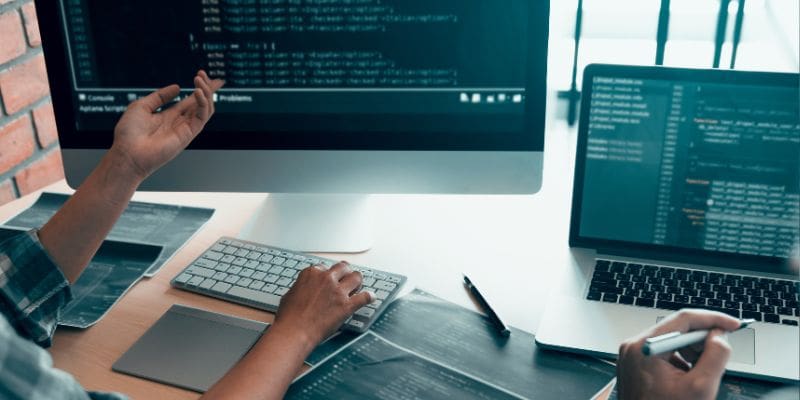 two people sitting working on two computers with code on the screen - penetration testing