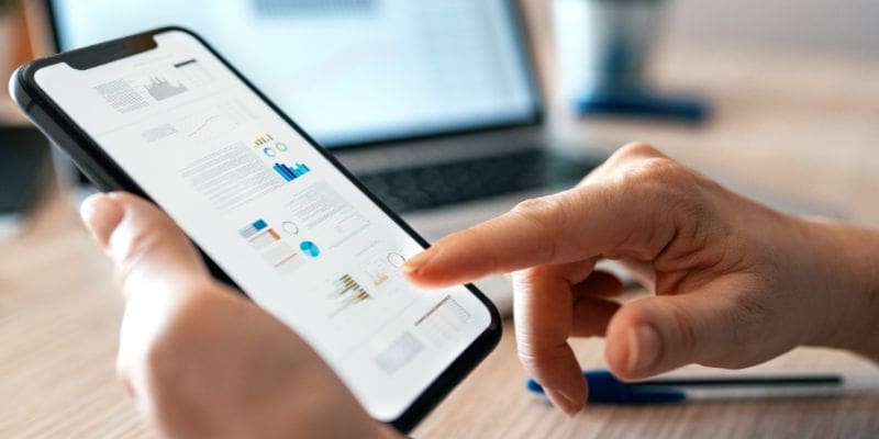 Person holding mobile phone touch screen with laptop in background